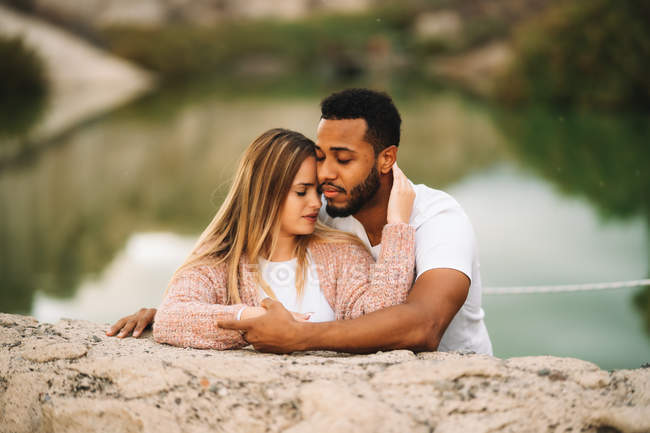 Happy casual multiracial couple with closed eyes embracing each other in nature — Stock Photo