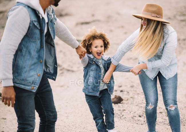 Cheerful parents holding hands with smiling adorable curly ethnic toddler — Stock Photo