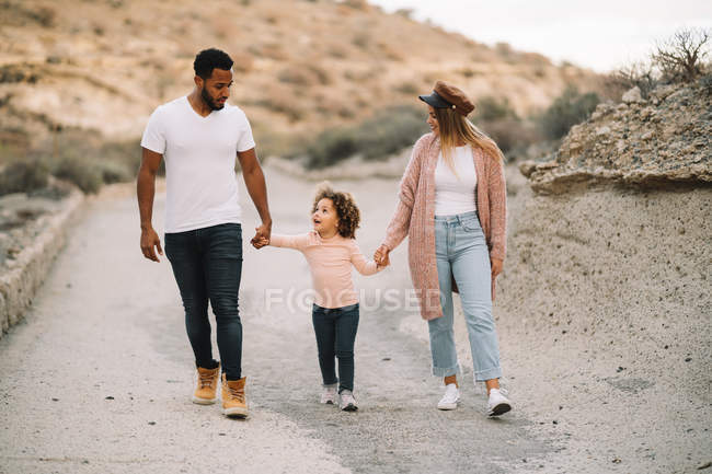Felice madre e padre diversificato con bambino riccio passeggiando sulla natura durante il giorno — Foto stock