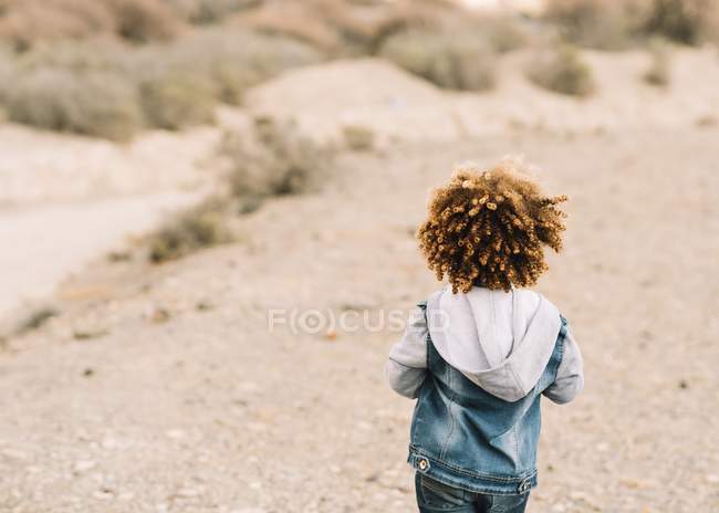 Задний вид кудрявого ребенка, одетого в повседневную одежду на размытом фоне — стоковое фото