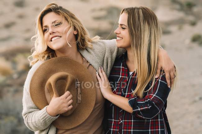Dos hermosas mujeres rubias abrazándose como descansando en el desierto durante el día - foto de stock