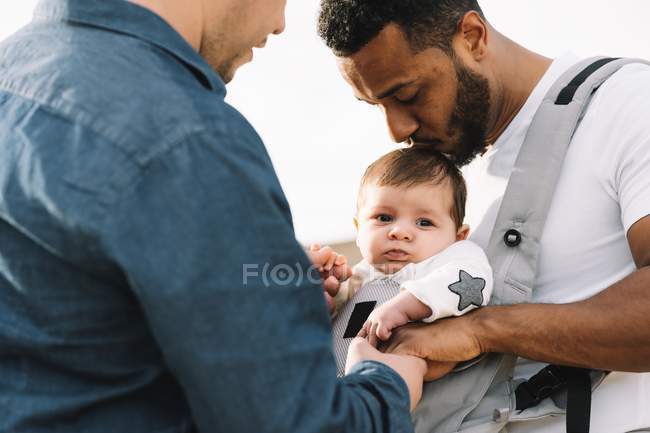 Pères multiraciaux câlins petit bébé en plein air — Photo de stock