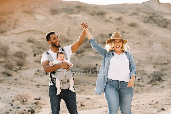 Fröhlicher Mann mit kleinem Baby und Händchen mit blonder Frau beim Wandern in sandiger Wüste — Stockfoto