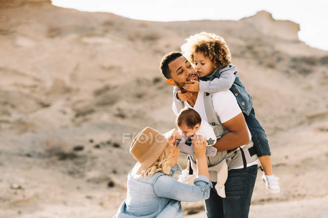Felice casuale moglie caucasica e nero sorridente marito che gioca con i bambini carini sulla natura durante il giorno — Foto stock