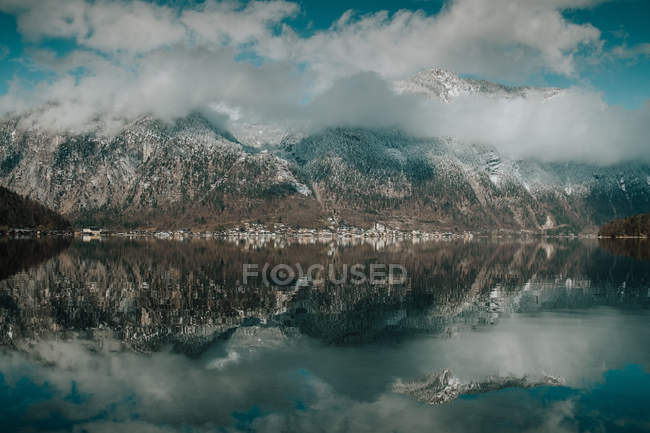 Serene stunning landscape of motionless lake reflecting bright cloudy sky surrounded by snowy mountains in Hallstatt — Stock Photo