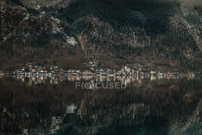 Paesaggio drammatico di lago trasparente circondato da montagne scure con alberi a Hallstatt — Foto stock