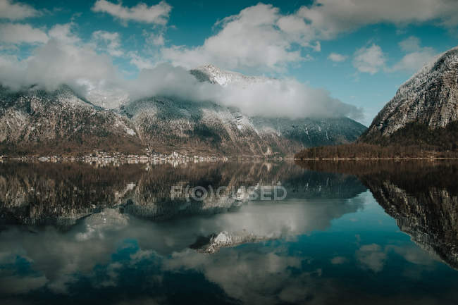 Serena paisagem deslumbrante de lago imóvel refletindo céu nublado brilhante cercado por montanhas nevadas em Hallstatt — Fotografia de Stock