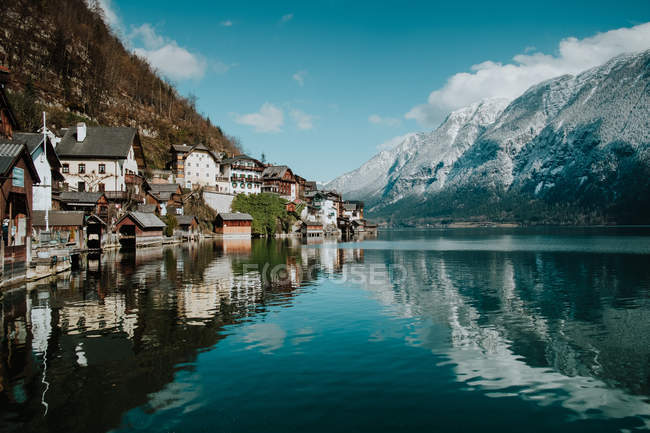 Splendide paysage de rivage pittoresque avec des bâtiments et des montagnes le long d'un lac cristallin calme reflétant ciel et nuages à Hallstatt — Photo de stock