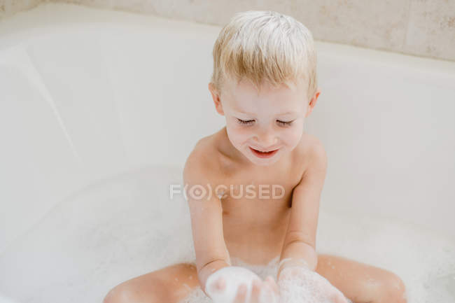 Miúdo bonito brincando com espuma no banho — Fotografia de Stock