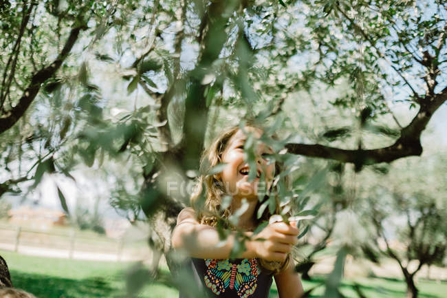 Улыбающаяся девушка залезает на дерево в солнечный день — стоковое фото
