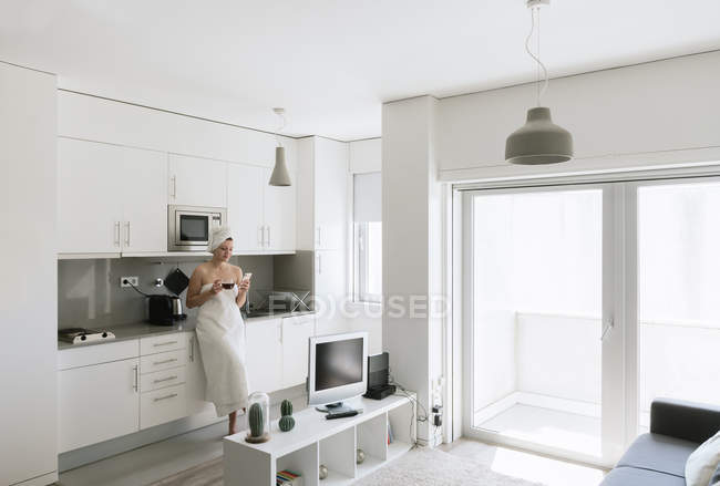 Joyful adult woman enjoying day off while having hot drink after bath in apartment with simple interior design — Stock Photo