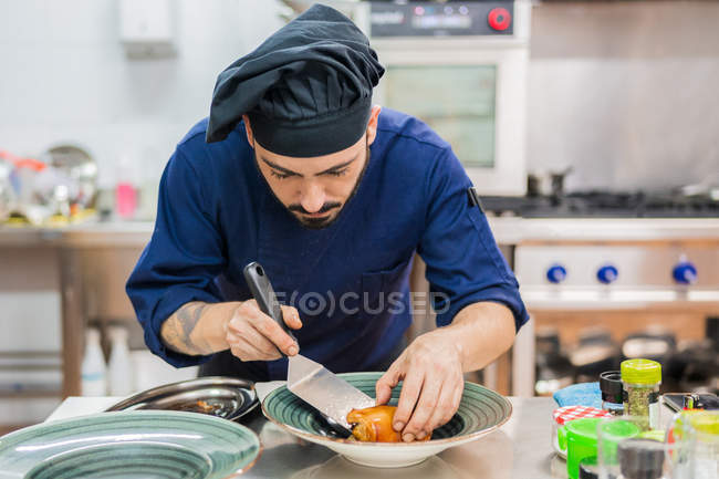 Орієнтований професійний чоловічий кухар використовує шпатель і кладе їжу на тарілку, готуючись до подачі на кухню ресторану — стокове фото