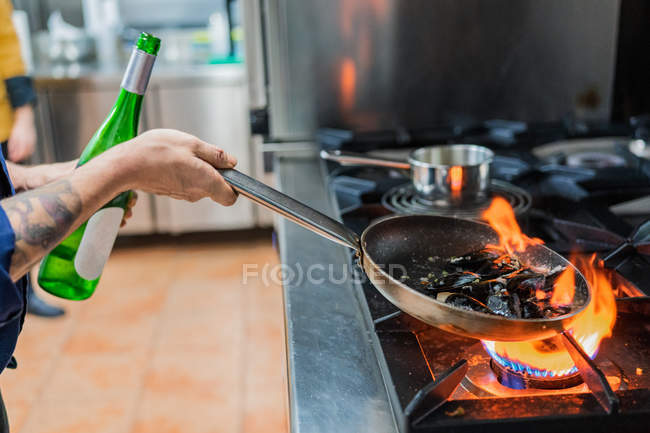 Cocinero cocinando con llama en sartén - foto de stock