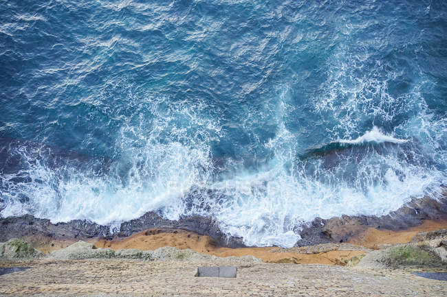 D'en haut du bord de mer sous la colline avec de l'eau turquoise et de la mousse sur les vagues à Naples en Italie — Photo de stock