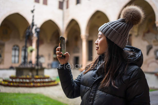 Азійська жінка-туристка в теплому одязі і капелюх фотографується на мобільному телефоні під час вивчення стародавньої базиліки Сан-Антоніо в Падові (Італія). — стокове фото