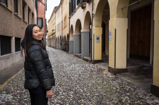 Viaggiatore femminile in abiti caldi che cammina su strada in pietra a blocchi tra bellissimi edifici storici a Padova guardando la macchina fotografica — Foto stock