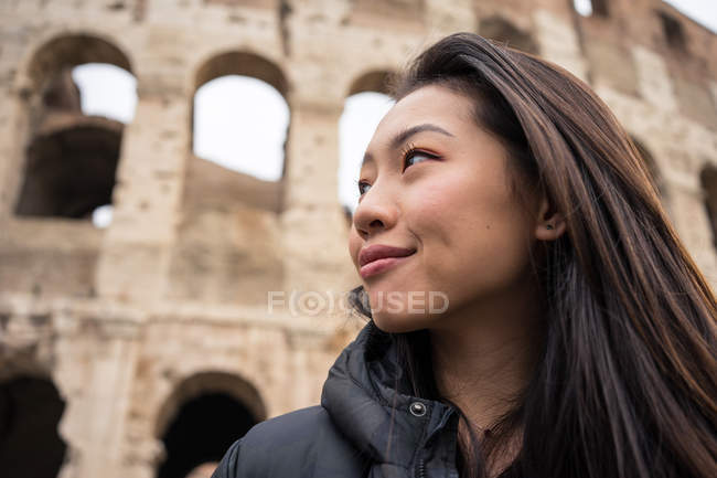 Von brüllend glückliche Frau lächelnd und wegschauend, während sie auf verschwommenem Hintergrund des Kolosseums auf der Straße von Rom, Italien steht — Stockfoto