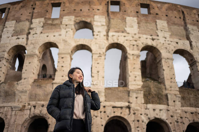 From bellow happy woman smiling and looking away while standing on blurred background of Colosseum on street of Rome, Italy — Stock Photo