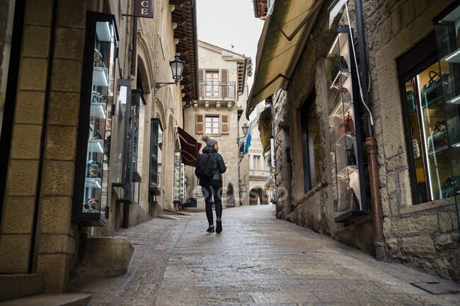 Vista posteriore della donna in giacca calda e cappello passeggiando per strada guardando attentamente le vetrine dei negozi a San Marino — Foto stock