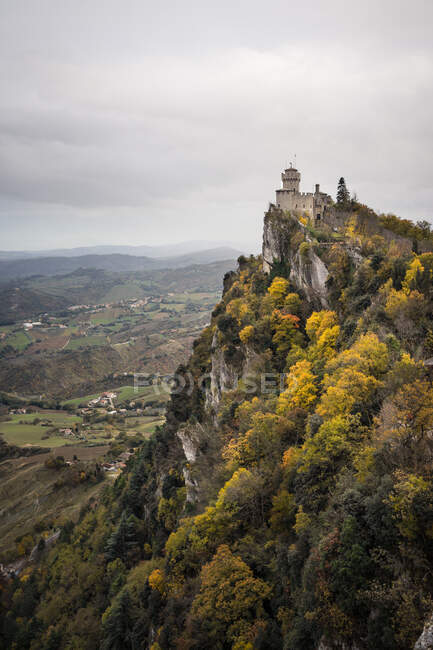 Antico castello in cima ricoperto da alberi verdi che si innalzano in cielo grigio a San Marino — Foto stock