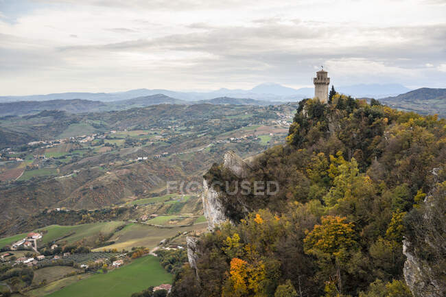 Antiguo castillo en el pico cubierto de árboles verdes que se elevan alto en el cielo gris en San Marino, Italia - foto de stock