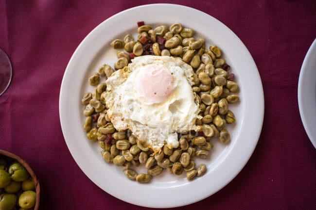 Сверху фасоль блюдо с жареным яйцом подается на тарелке на красной скатерти в ресторане Малаги — стоковое фото