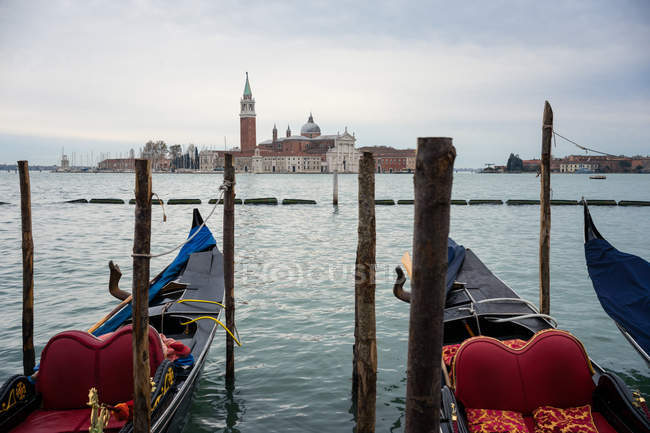 Gondolas on blue water on wharf with historical old buildings and cloudy sky on background — Stock Photo