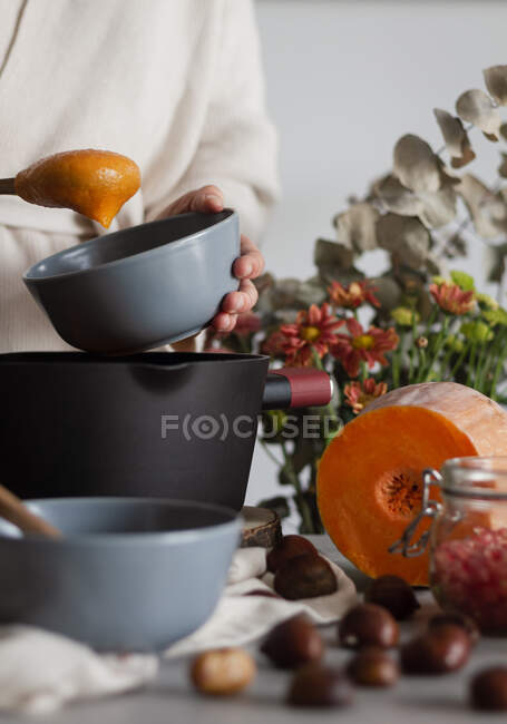 Crop cook with soup bowl and spoon in hands cooking pumpkin and chestnut cream soup — Stock Photo