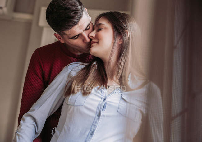 Pregnant woman with husband looking at window at home — Stock Photo