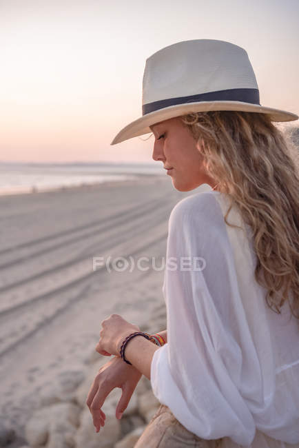 Charming woman in hat leaning on fence and looking at sea — Stock Photo