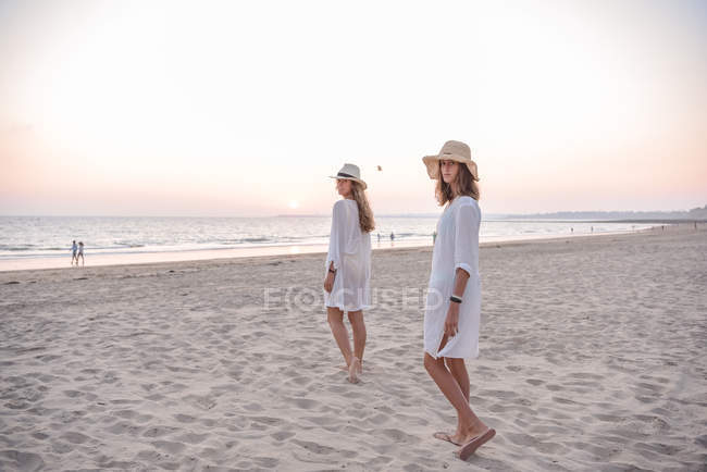 Усміхнені подружки в літньому одязі босоніж у воді на пляжі — стокове фото