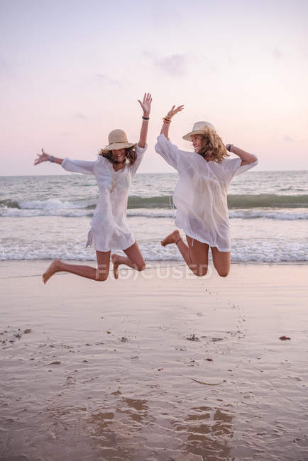 Sonrientes novias en ropa de verano descalzas en el agua en la playa - foto de stock