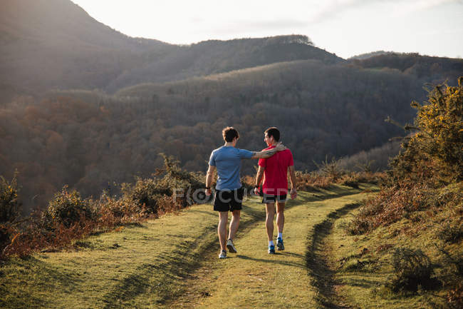 Adult athletic men resting walking on grass trail post running training in mountains in sunny day — Stock Photo