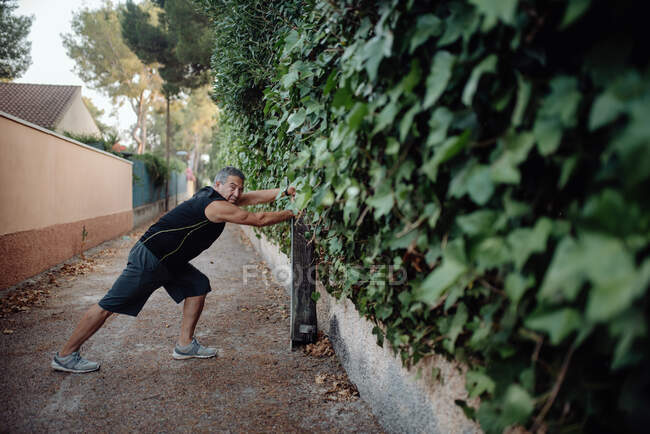Літній чоловік тягнеться на ботанічну стіну на вулиці — стокове фото