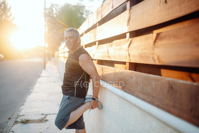 Elderly man stretching on wooden wall in street — Stock Photo