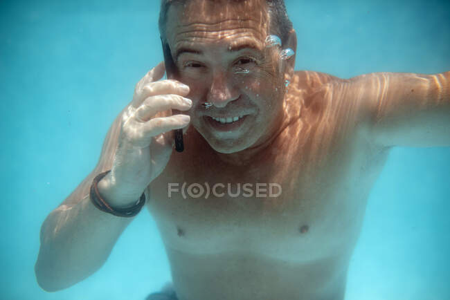 Homme mûr plongeant sous l'eau avec smartphone — Photo de stock