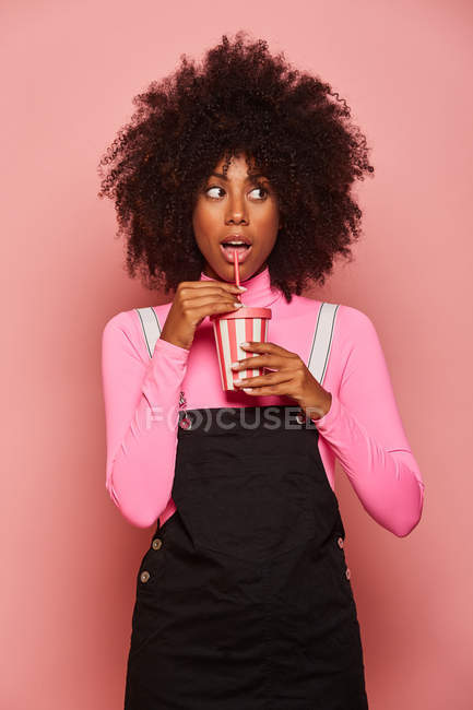 Счастливая чернокожая женщина с одноразовой чашкой напитка на розовом фоне — стоковое фото