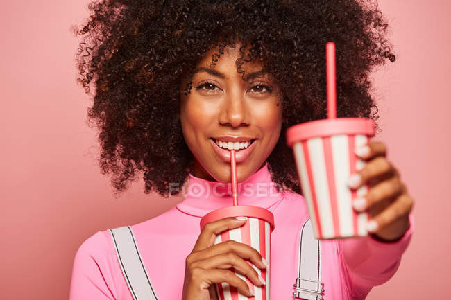 Happy black woman with disposable cup of drink standing against pink background — Stock Photo