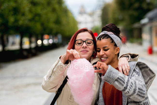 Enthusiastic multiracial friends hugging and eating cotton candy in park — Stock Photo