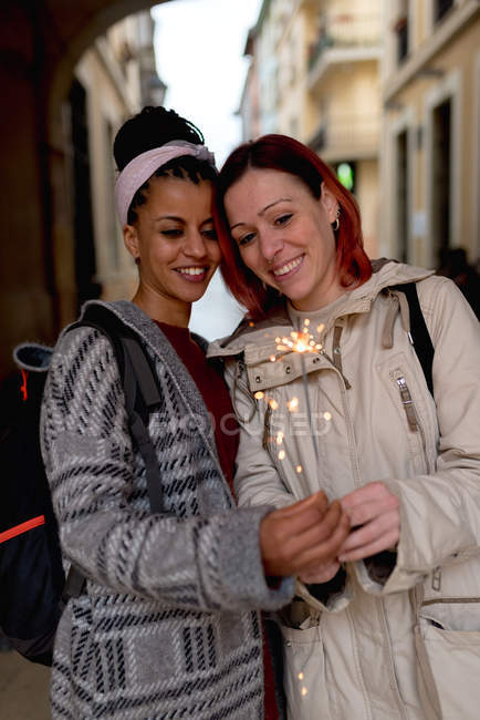 Sorridente donne multirazziali in piedi e tenendo sparkler in fiamme — Foto stock