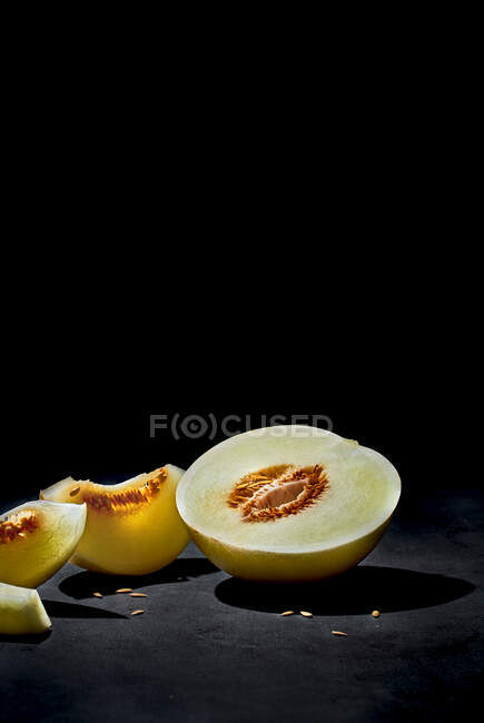 Bisected ripe fresh melon with seeds and tasty pieces under light in dark room — Stock Photo
