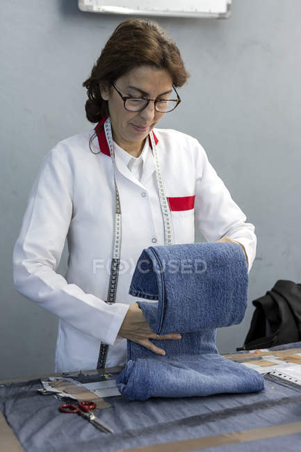 Mulher trabalhadora em fábrica têxtil verificando a qualidade das peças de vestuário. Produção industrial — Fotografia de Stock