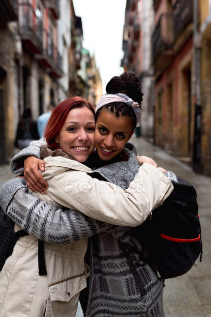 Content multiracial girl friends embracing in narrow street — Stock Photo