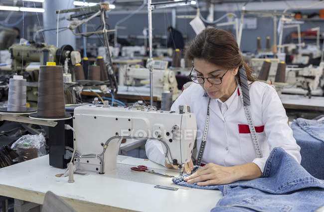 Робоча жінка на текстильній фабриці шиє на промисловій швейній машині. Промислове виробництво — стокове фото