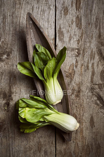Top view of ripe bok choy placed near wooden plate on shabby lumber table in kitchen — Stock Photo