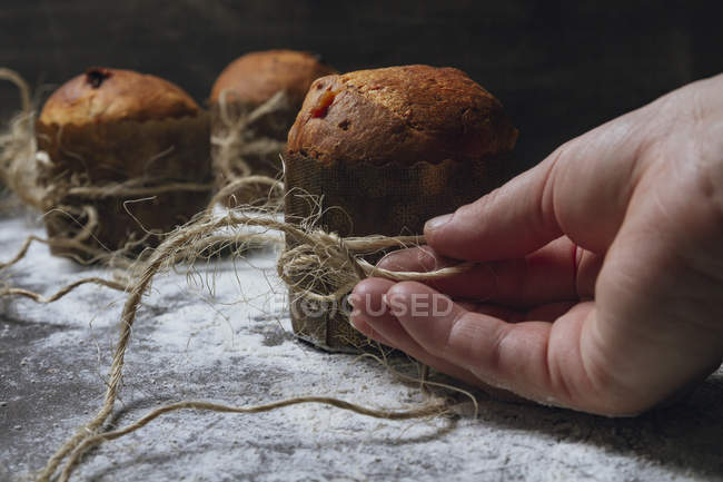 Hand of person arranging twine on fresh baked homemade Christmas cakes placed on table powdered with white flour — Stock Photo