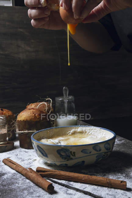 Hände der Person brechen Ei in Schüssel auf Holztisch mit Zimt und Vanille und gebackenen Kuchen platziert — Stockfoto