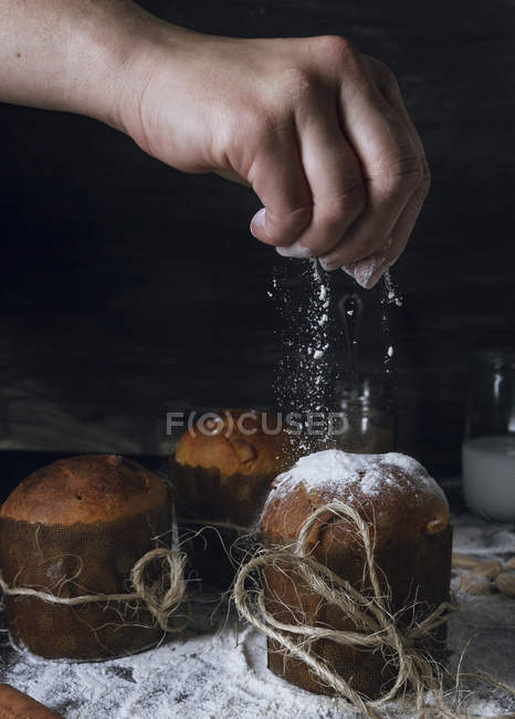 Рука человека, посыпающего сахарной пудрой свежий домашний итальянский рождественский торт, украшенный бечевкой — стоковое фото