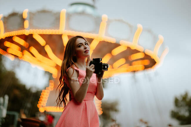 Mujer milenaria tomando fotos con cámara en el parque de atracciones - foto de stock