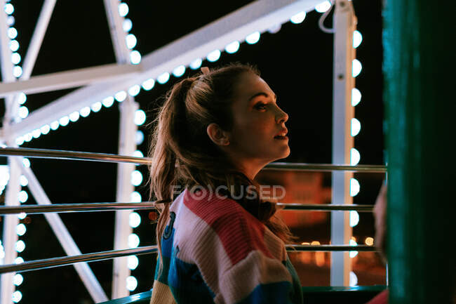 Young woman riding luminous Ferris wheel in summer night — Stock Photo